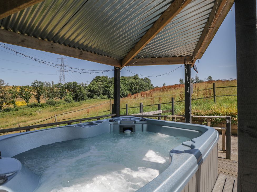 A hot tub under a canopy with a view of fields at Hedgehogs Lodge South Molton