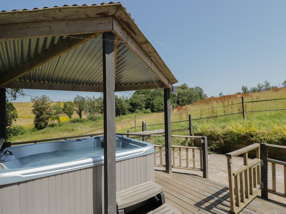 A hot tub on a wooden deck with grass in the background at Hedgehogs Lodge South Molton