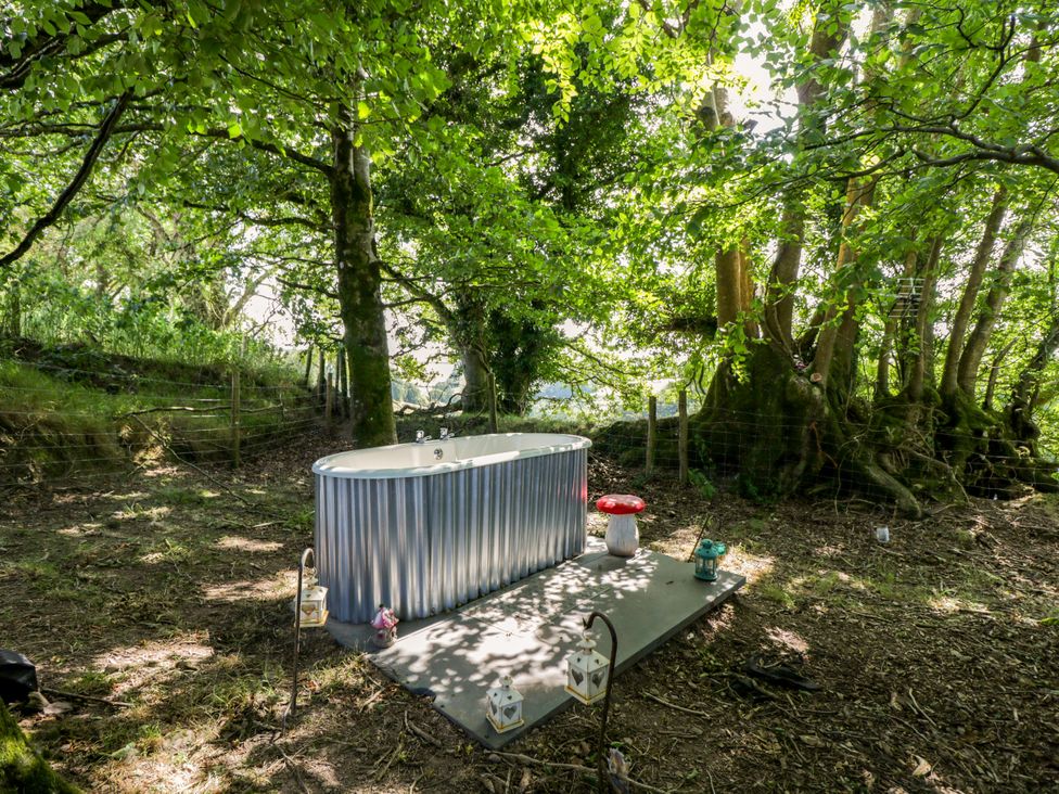 A bathtub placed on a concrete base in a forested outdoor area at Valley View Shepherd's Hut in South Molton