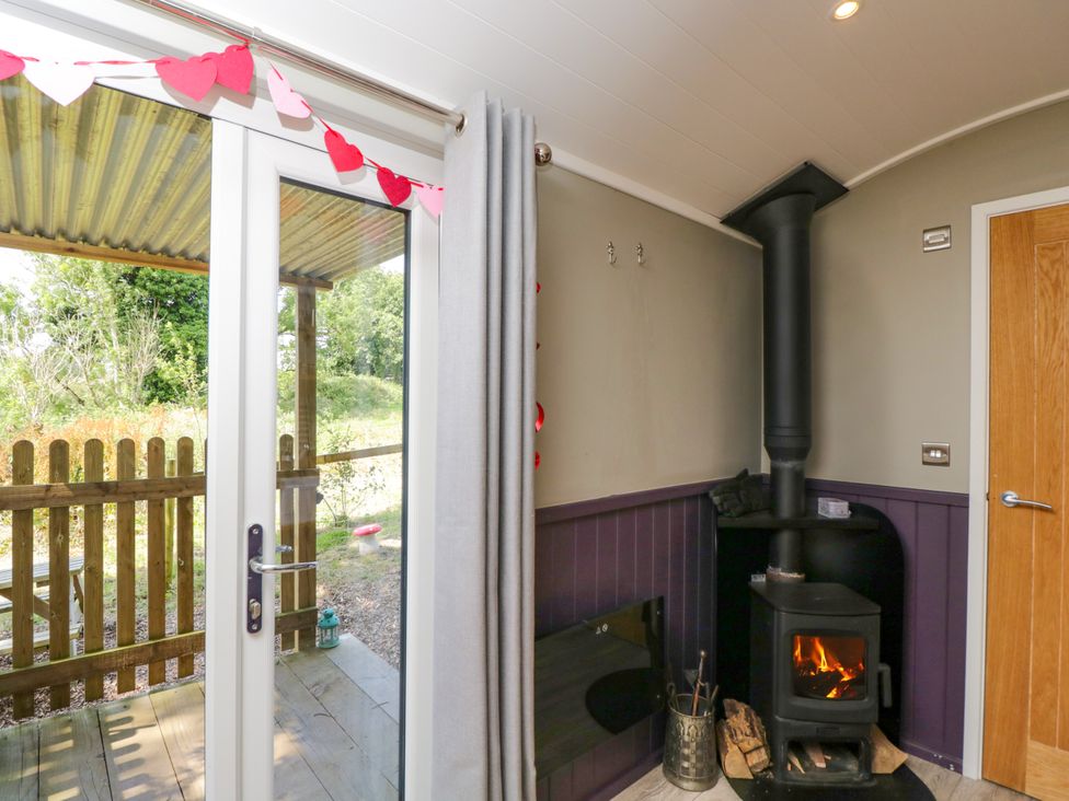 A living room with a stove and door leading outside at Valley View Shepherd's Hut in South Molton