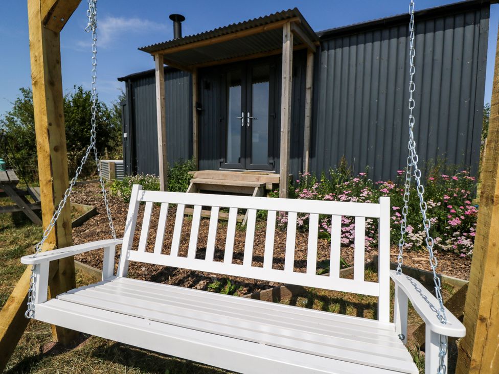 A swing bench with a building in the background at Hares Hideaway Shepherd's Hut South Molton