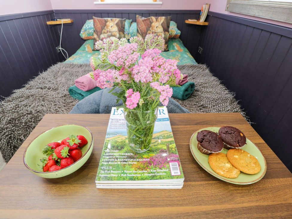 A bedroom with a bed, flowers, fruits, and snacks at Hares Hideaway Shepherd's Hut in South Molton