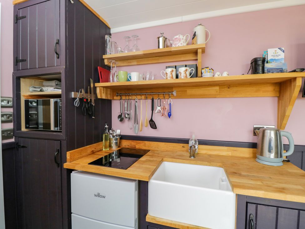 A kitchen with cabinets, stove, sink, and utensils at Hares Hideaway Shepherd's Hut in South Molton