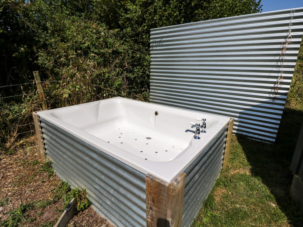 A hot tub with faucets surrounded by corrugated metal in the garden at Hares Hideaway Shepherd's Hut South Molton