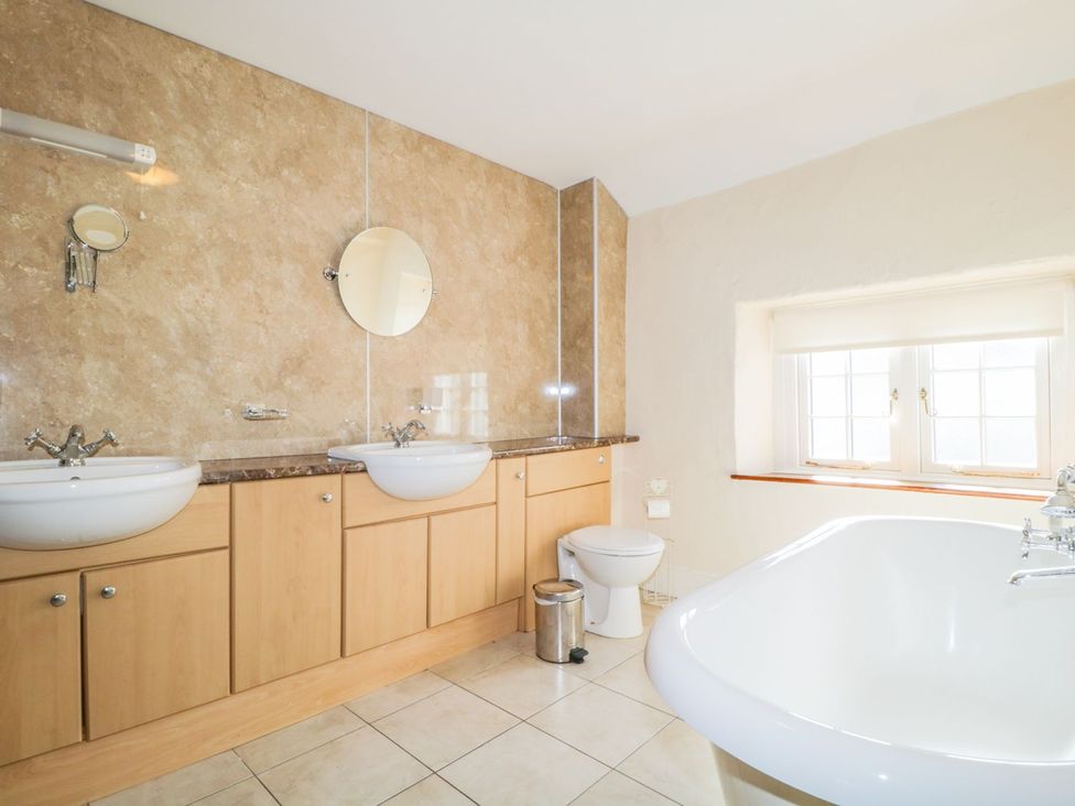 A bathroom with two sinks, toilet, bathtub, and window at The Farmhouse in Keswick
