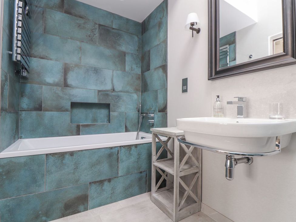 A bathroom with a bathtub and wall-mounted sink at Wood Meadow in Helston