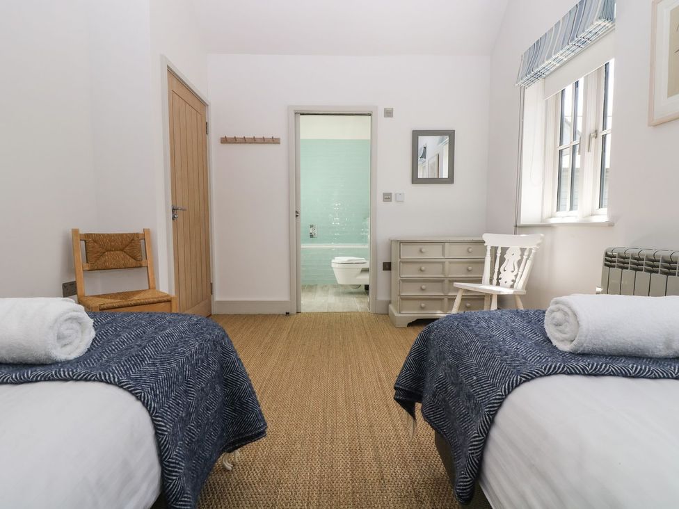 A bedroom with two beds and a door leading to a bathroom at Wood Meadow in Helston
