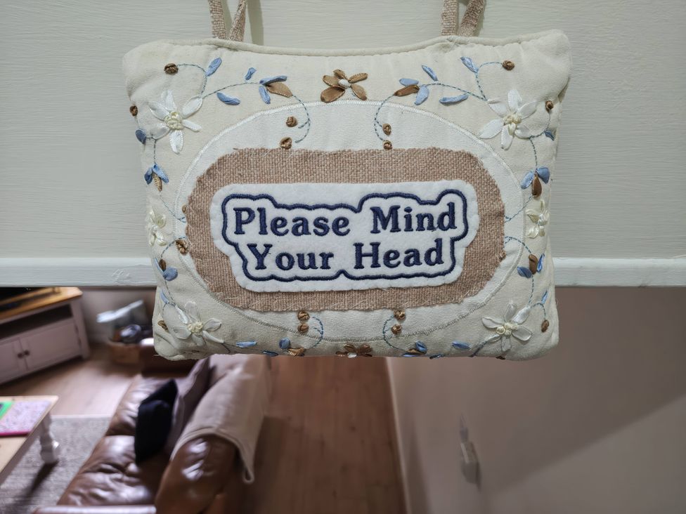 A sign reading 'Please Mind Your Head' with floral embroidery at Bobbin Nook in Staveley