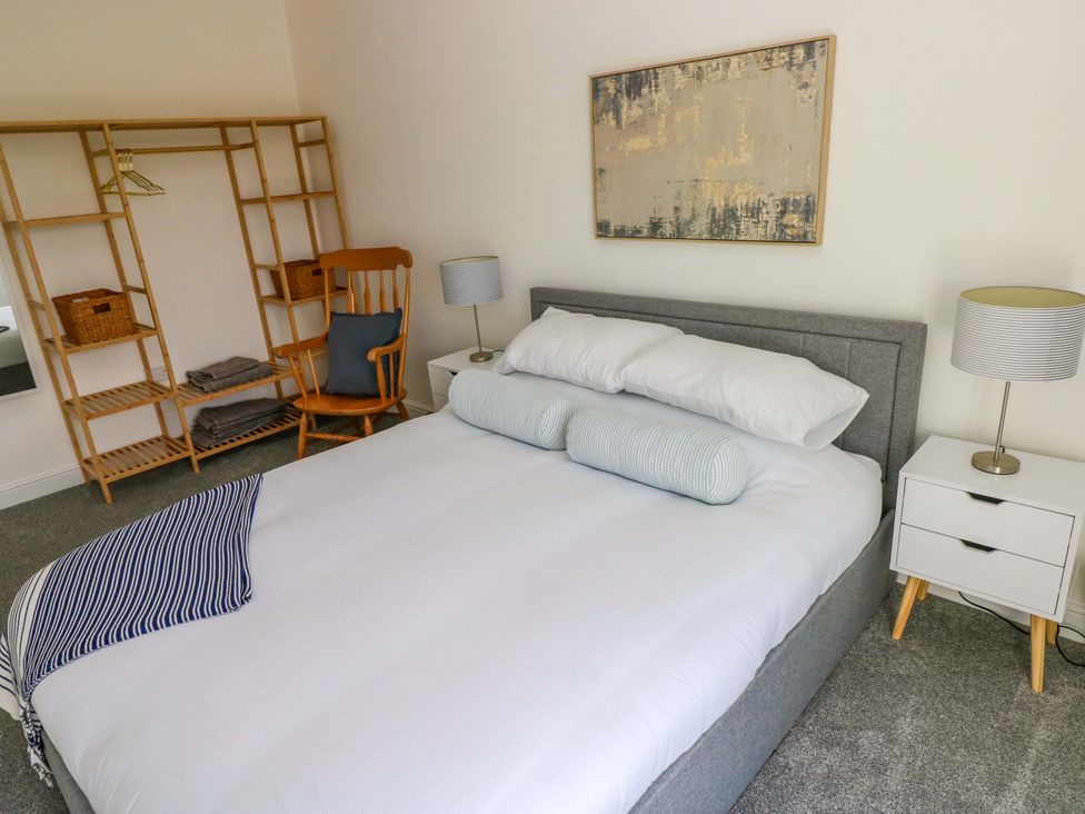 A bedroom with a bed, nightstand, lamp, rocking chair, and shelves at Mountain View Cottage in Ystradgynlais