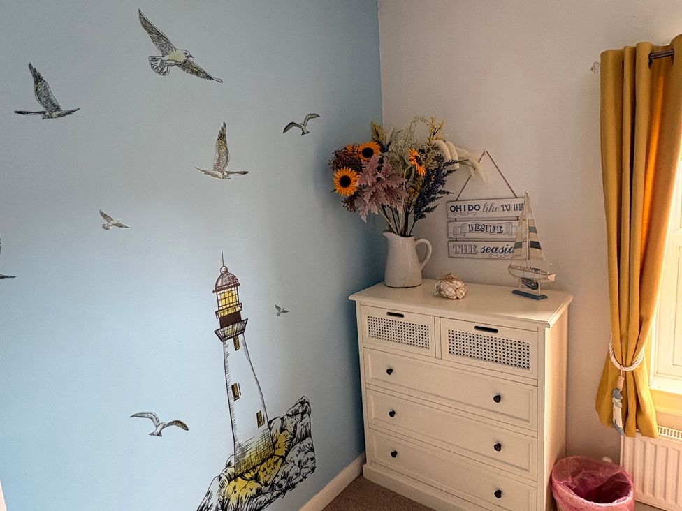 A bedroom with a lighthouse mural and a dresser featuring flowers and decorative items at Hideaway Cottage Hunstanton