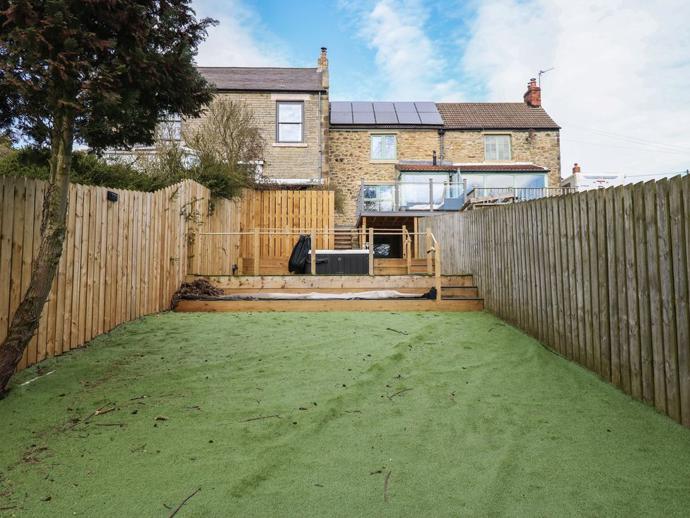 A garden with artificial grass and steps leading to a hot tub at 2 Low Road