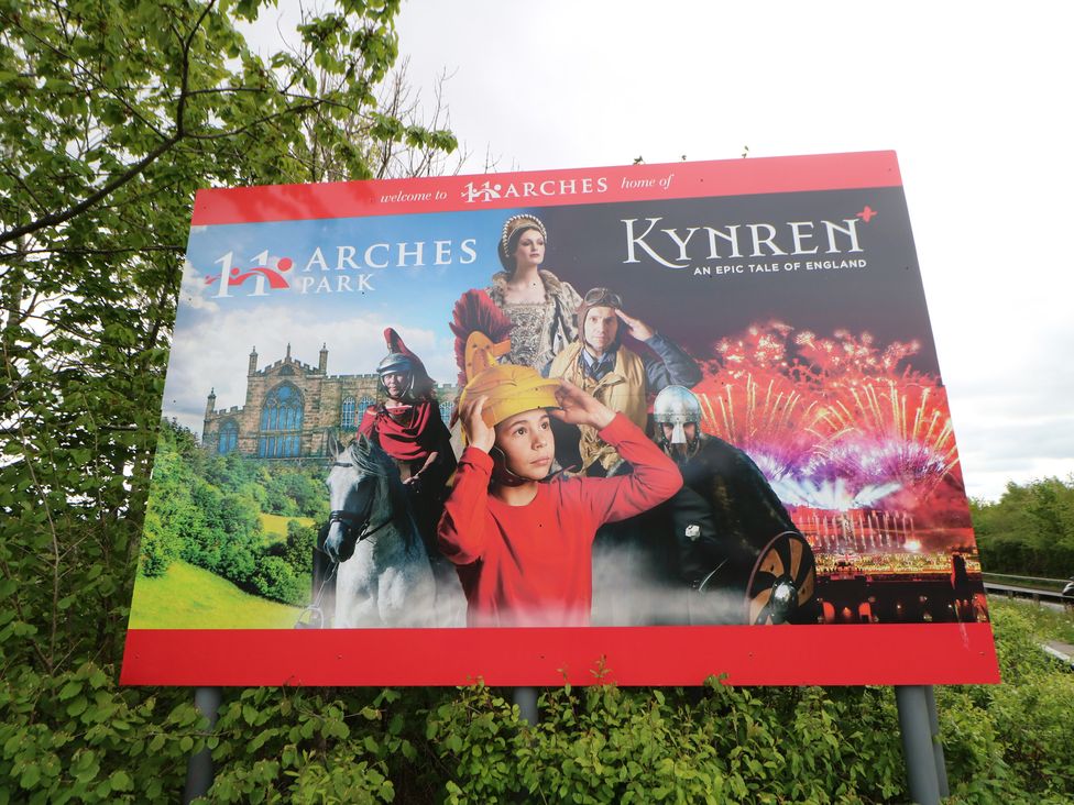 A promotional sign for Kynren at Arches Park featuring characters and fireworks