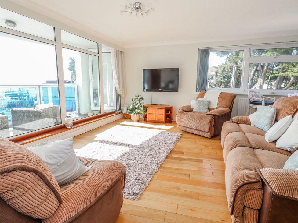 A living room with a sofa, armchairs, television, and large windows at Flat 17 Golden Gates in Poole