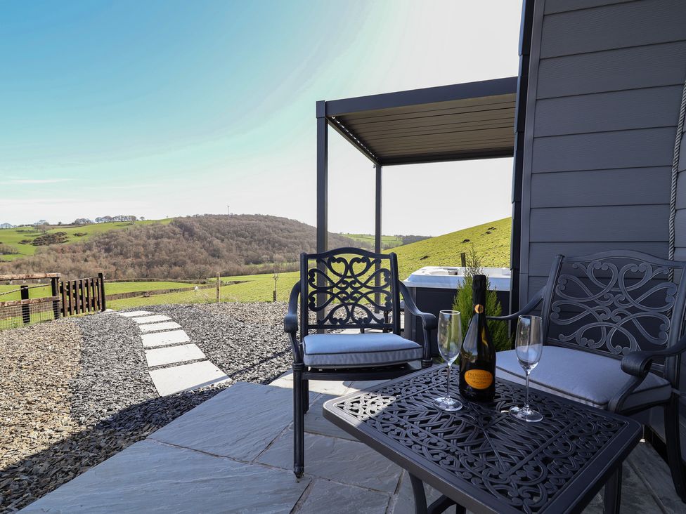 An outdoor patio with seating and a bottle on the table at Cennin Pedr in Ruthin
