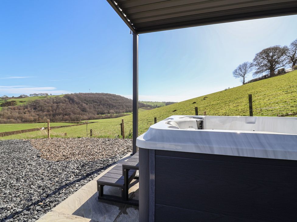 A hot tub with steps and gravel overlooking hills at Cennin Pedr in Ruthin