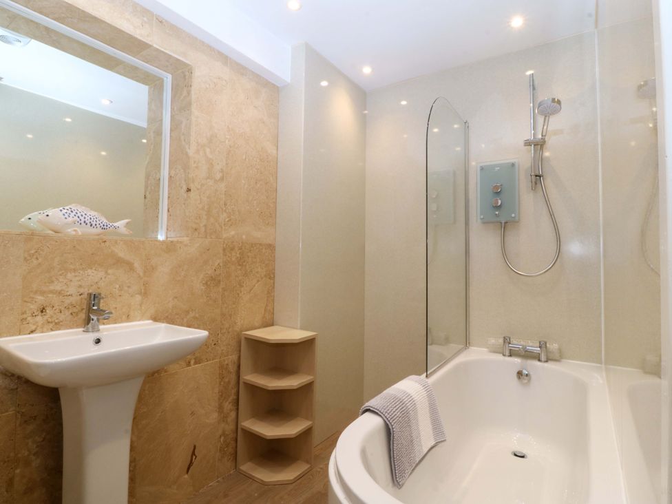 A bathroom with a bathtub, shower, sink, and shelving at 5 Ger Afon in Llanbedrog