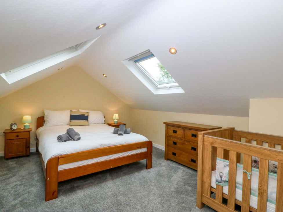 A bedroom with a bed, bedside table, lamp and crib at 5 Ger Afon in Llanbedrog