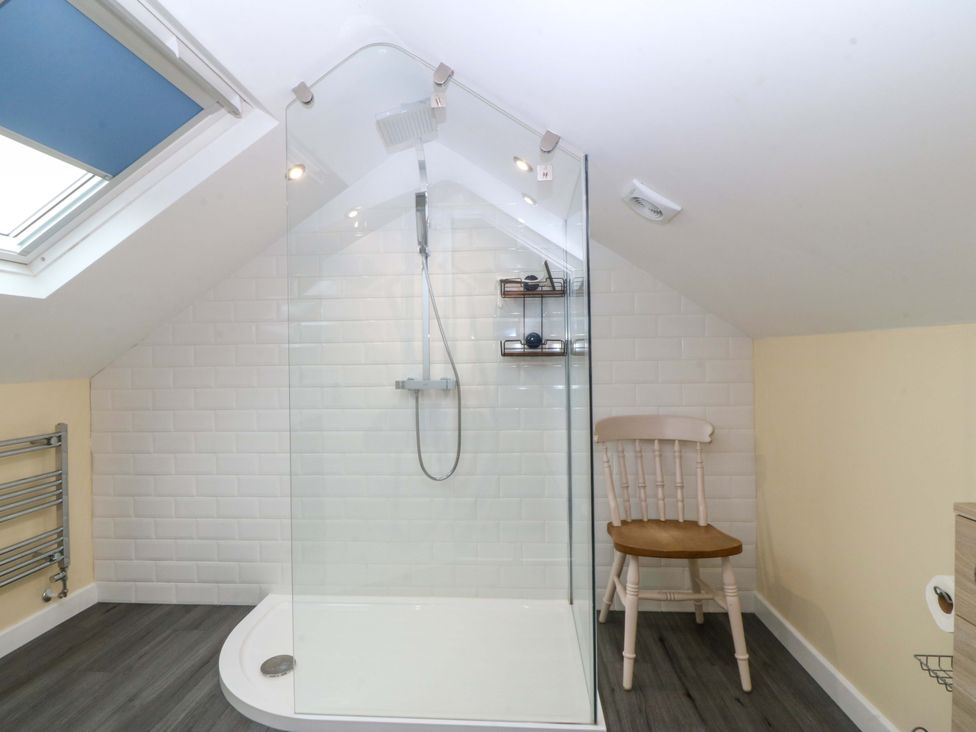 A bathroom with a shower and a chair at 5 Ger Afon Llanbedrog