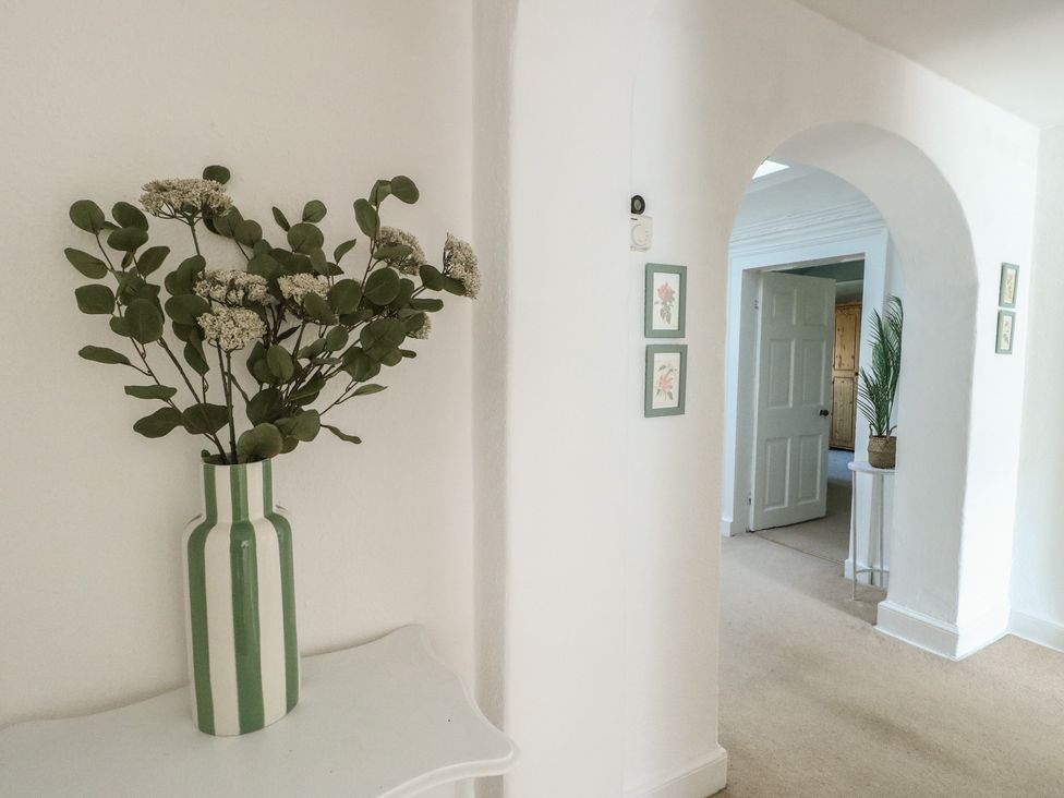 A hallway with a vase of flowers and picture frames at Castle Gardens Apartment Beaumaris