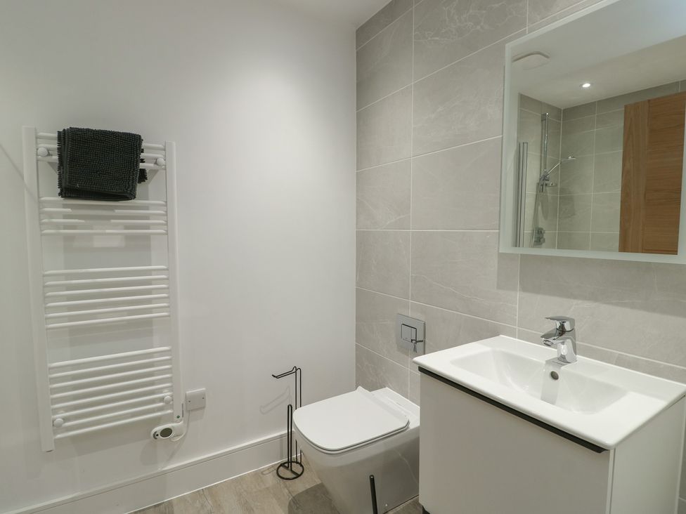 A bathroom with a sink, toilet, towel radiator and mirror at Glynllifon 5 in Marian-glas near Benllech