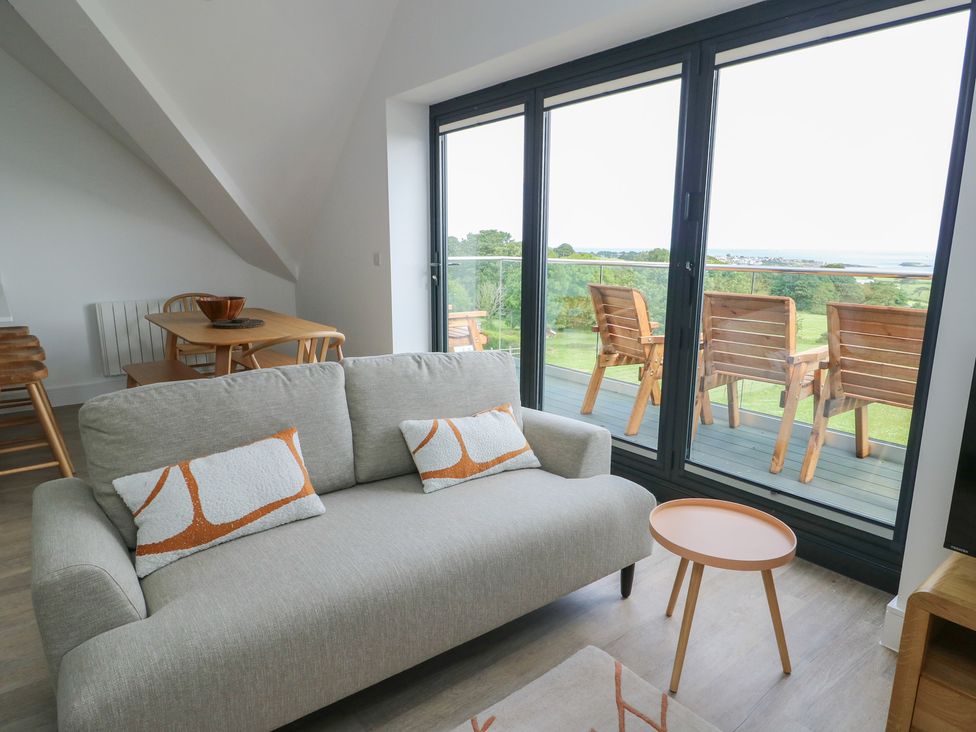 A living room with a sofa, table and balcony view at Glynllifon 8 Marian-glas near Benllech