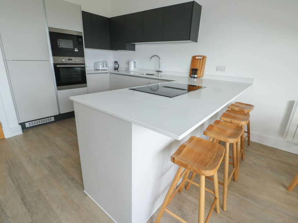 A kitchen with a countertop, sink, stove, and bar stools at Glynllifon 8 Marian-glas near Benllech