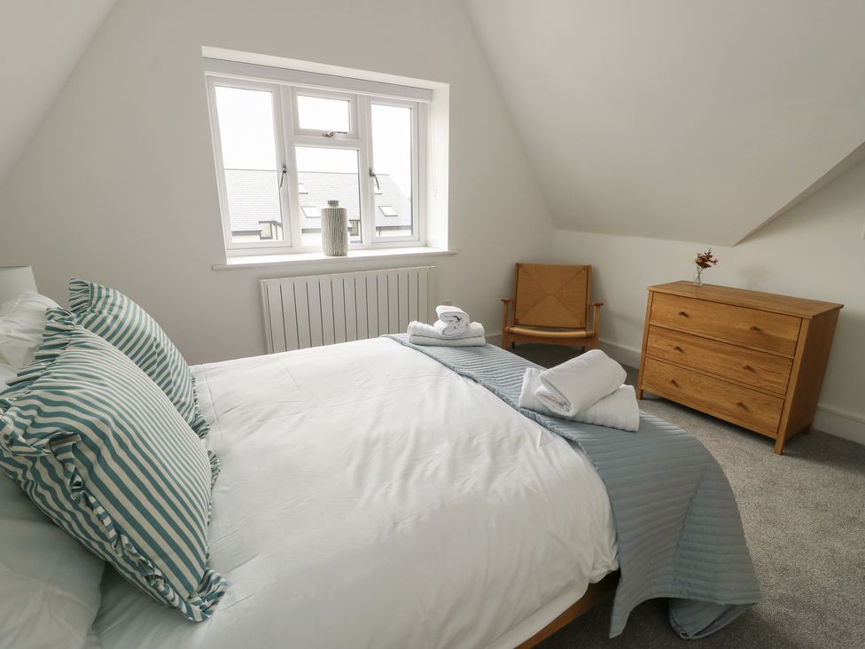 A bedroom with a bed, chair, dresser and window at Glynllifon 8 in Marian-glas near Benllech