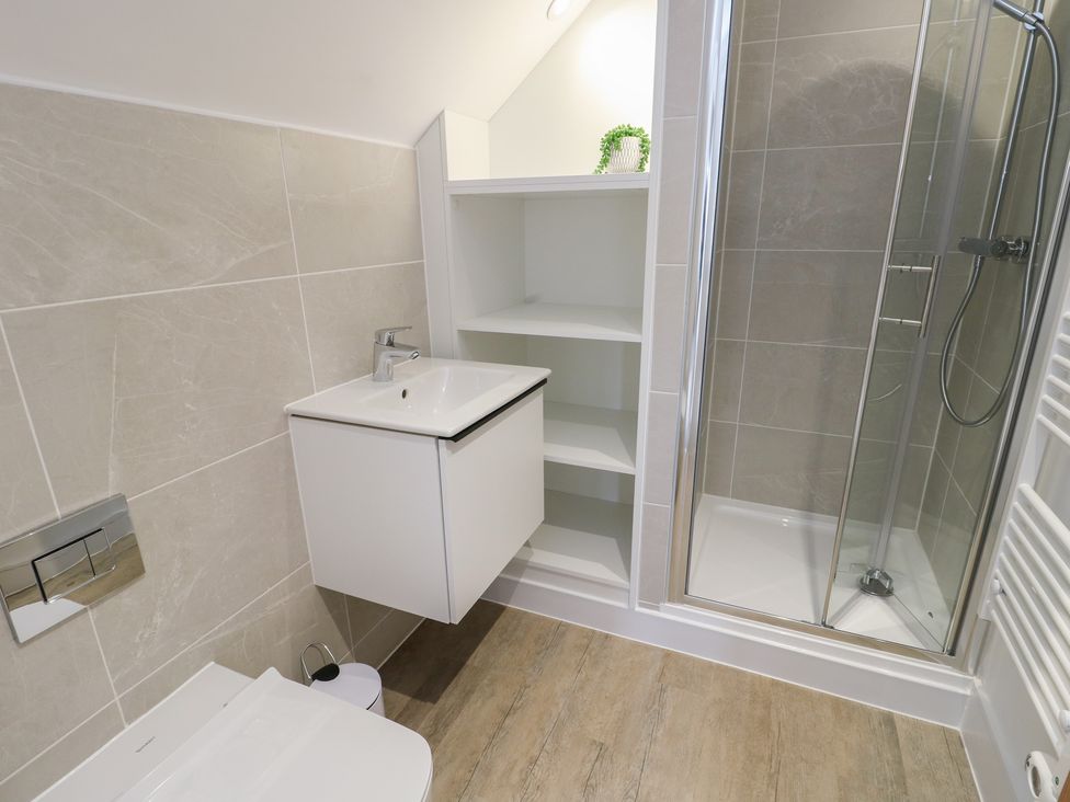 A bathroom with a sink, toilet, shower and storage shelf at Glynllifon 8 Marian-glas near Benllech