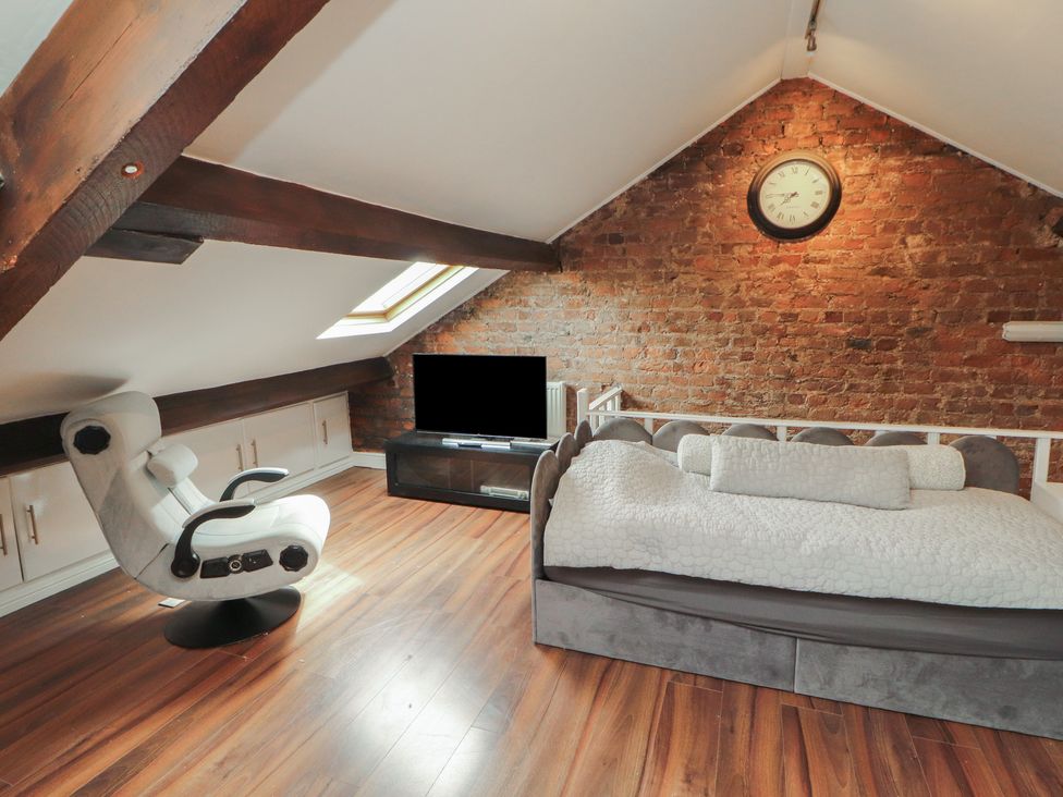 An attic room with a bed, chair, and television at Sugar Loft in Silloth
