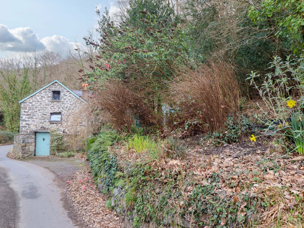A stone house beside a road with bushes and flowers at Millers Loft in Llanrwst