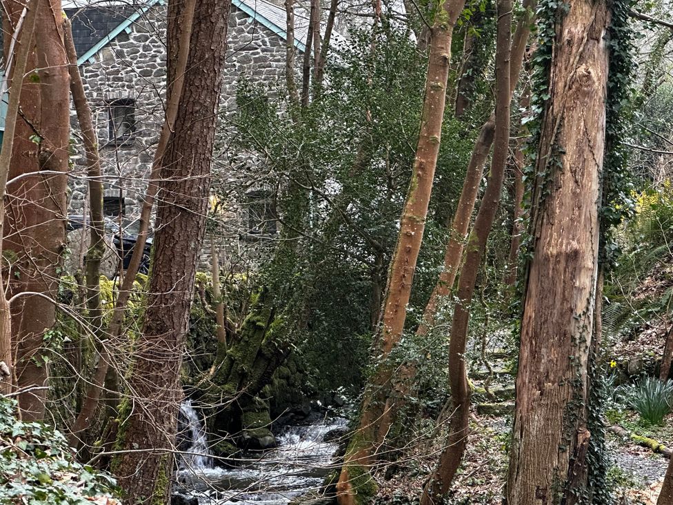 A view of trees and a stream near a stone building at Millers Loft in Maenan near Llanrwst