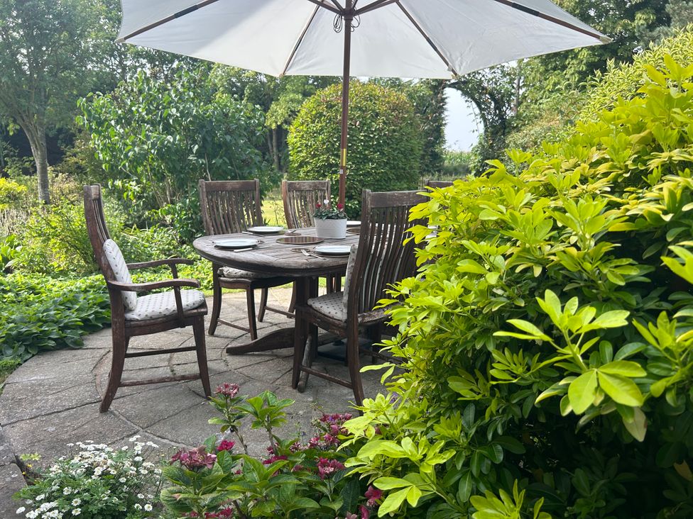 A garden with a wooden table and chairs under an umbrella at Cutbush Farmhouse in Norwich