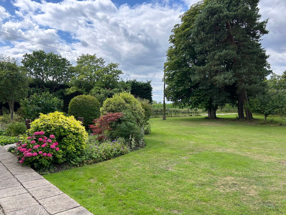 A garden with flower beds and trees at Cutbush Farmhouse in Norwich