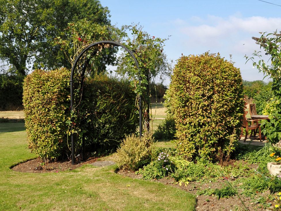 A garden with an archway and hedges at Cutbush Farmhouse in Norwich