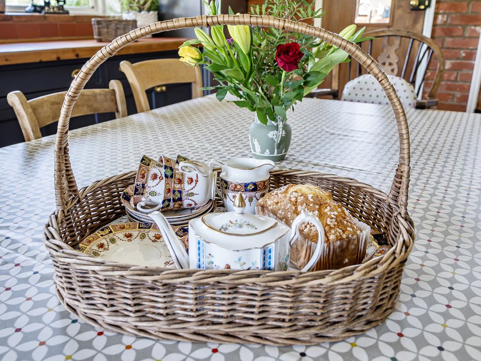A basket with teacups, a milk jug, a cake, and flowers at Cutbush Farmhouse, Hingham