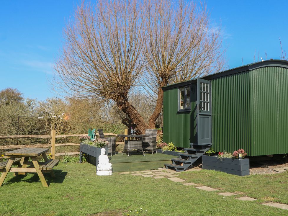 A garden with a shepherd's hut, table, chairs, and a tree at Salt Haven Shepards Hut Pevensey