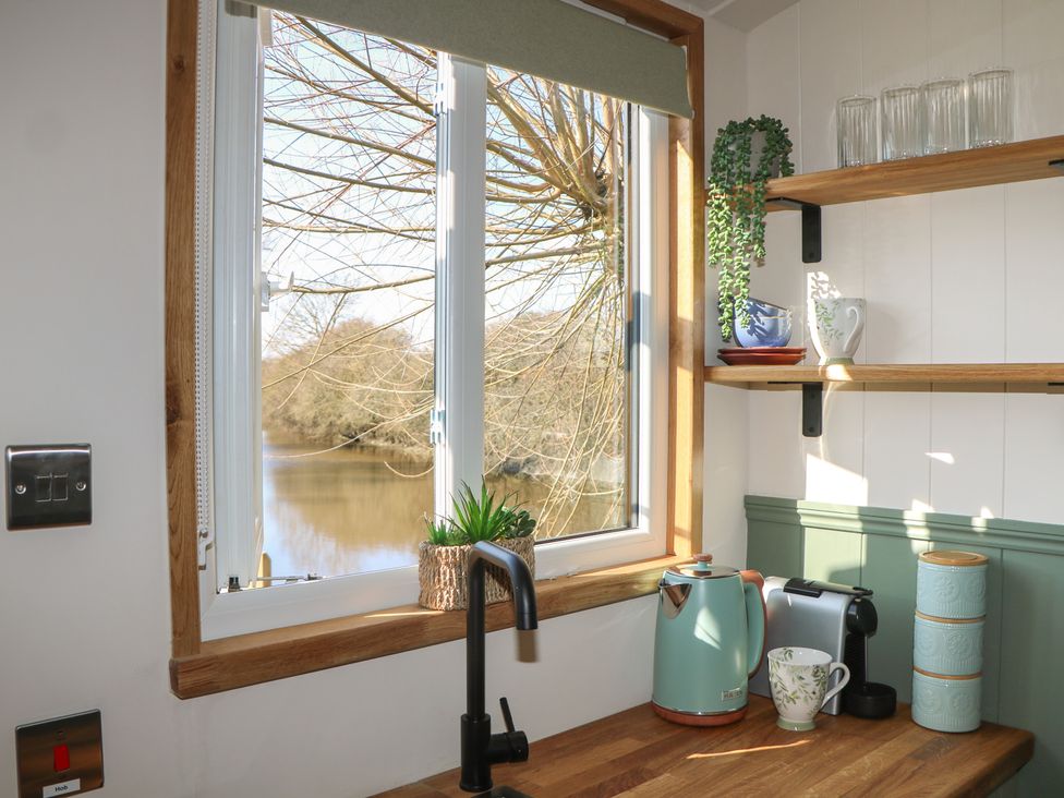 A kitchen featuring a window, tap, kettle and shelves at Salt Haven Shepards Hut Pevensey