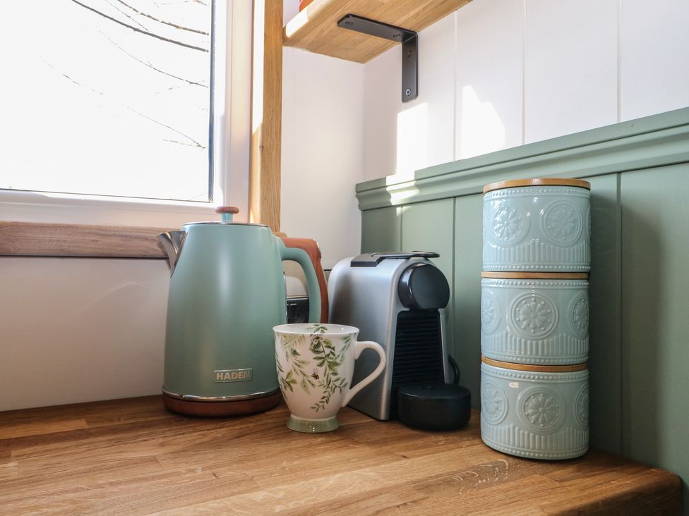 A kitchen counter with a kettle, cup, coffee machine, and storage containers at Salt Haven Shepards Hut Pevensey