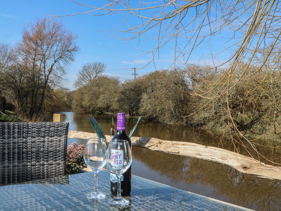 An outdoor area with a table, bottle, and glasses overlooking a river at Salt Haven Shepards Hut Pevensey