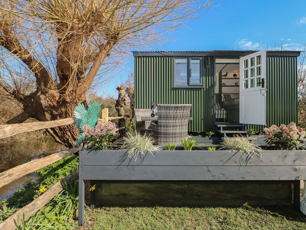 An outdoor view of a shepherd's hut with a chair and flower bed at Salt Haven Shepards Hut Pevensey