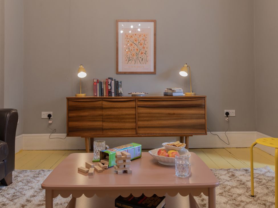 A living room with a sideboard and a table with books and a bowl of apples at The Clarence in Bishop Auckland