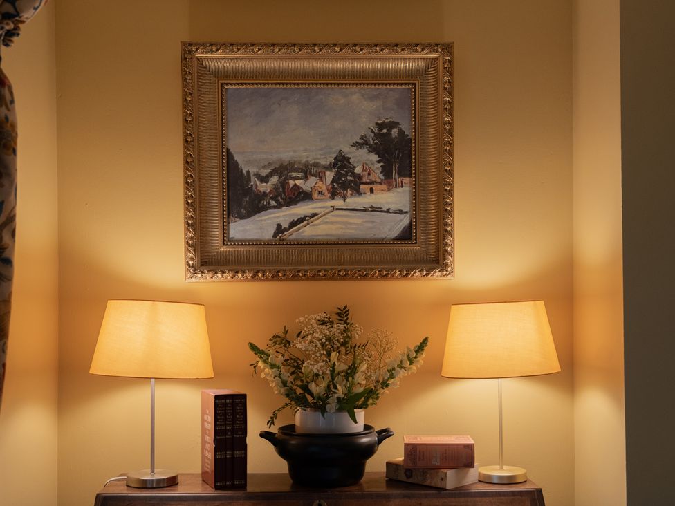 A living room with a painting, table lamps, and books at Churchill Cottage, Bishop Auckland