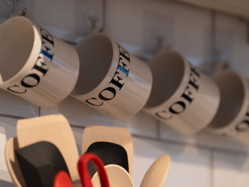 A row of coffee mugs hanging on kitchen hooks with utensils at Churchill Cottage Bishop Auckland