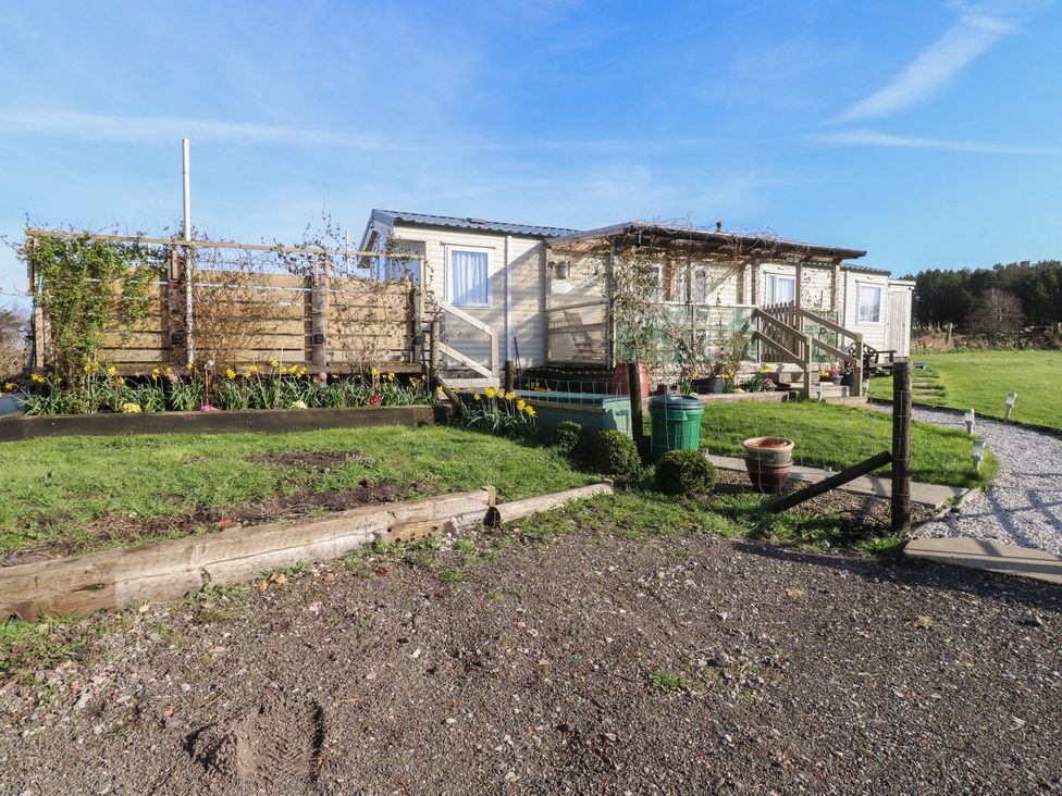 A mobile home with flower beds and fencing at Cornholme Lodge in Accrington