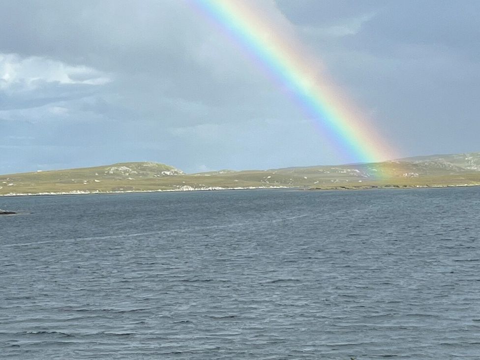 A landscape with a rainbow over water and hills at 3 Linshader in Stornoway