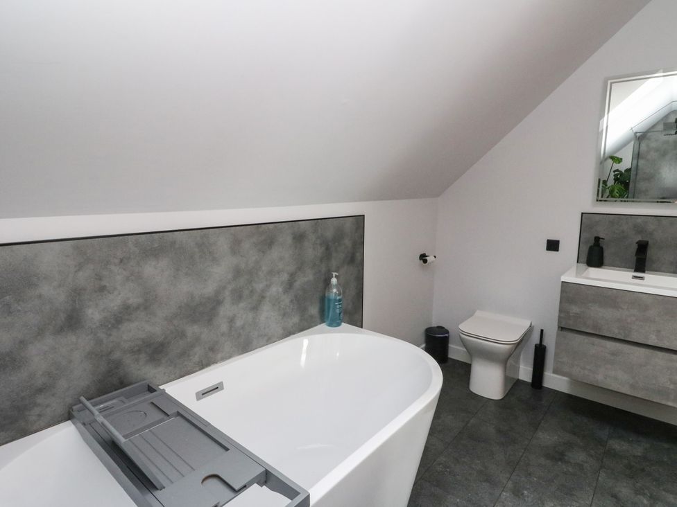 A bathroom with a bathtub, toilet, sink, and mirror at 3 Linshader in Stornoway