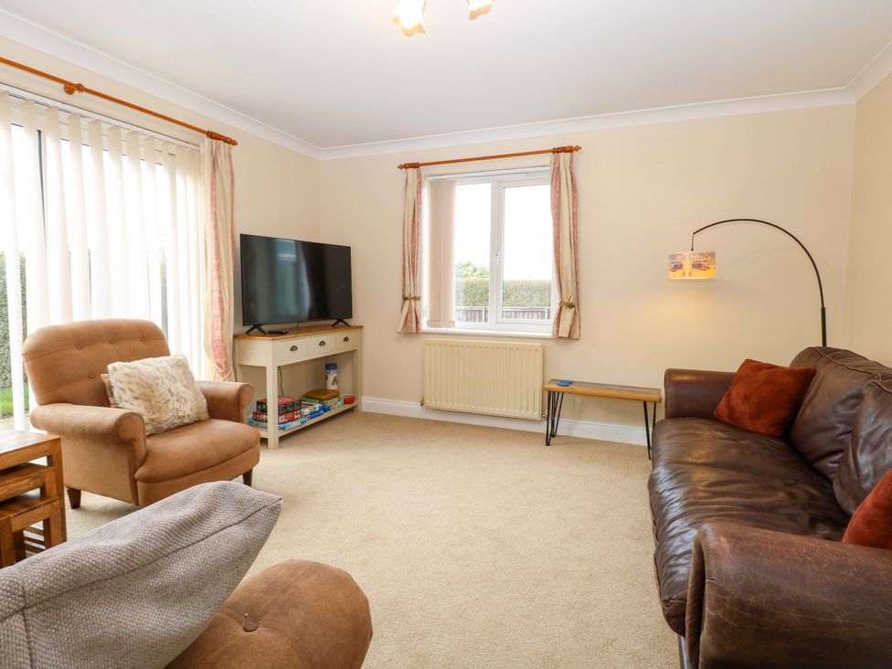 A living room with a sofa, armchair, television, and coffee table at The Bungalow in 