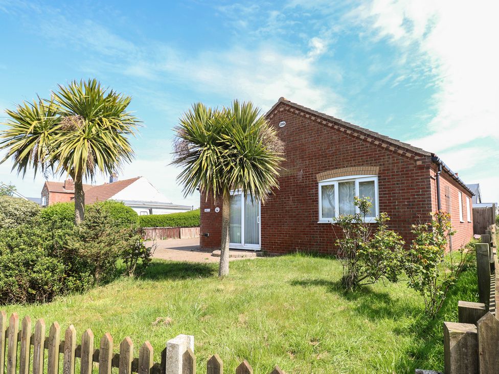 A brick house with palm trees and a garden at The Bungalow in Walcott