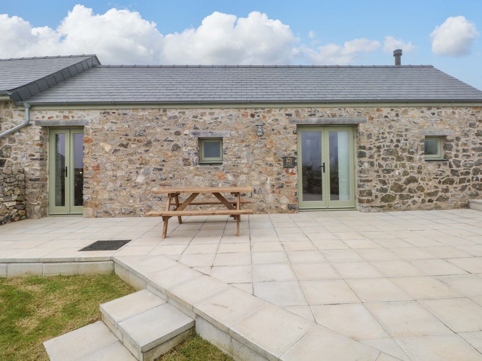 An outdoor area with a stone wall and wooden table at Dairy Cottage in Oxwich