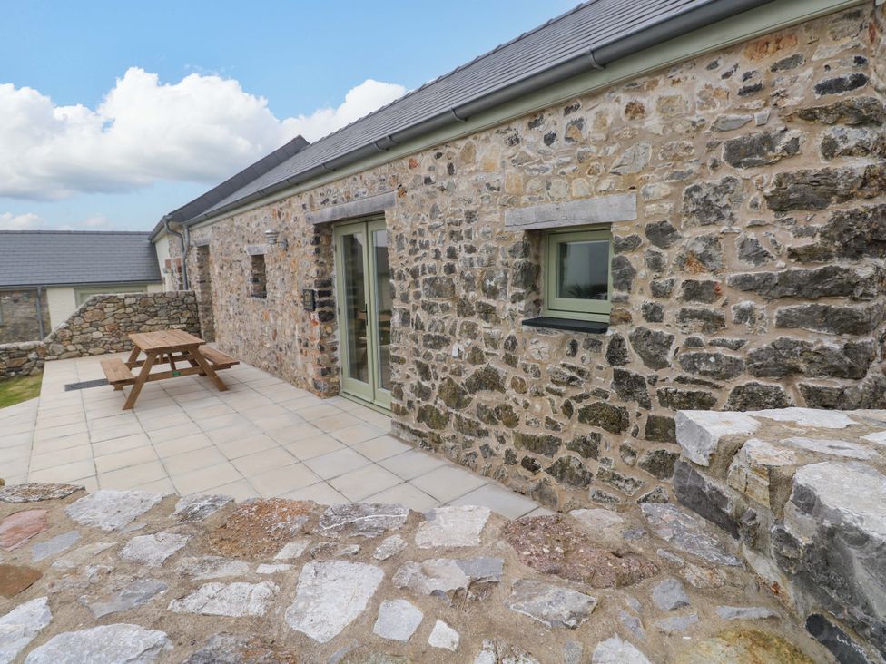 An outdoor area with a stone wall and wooden table at Dairy Cottage in Oxwich